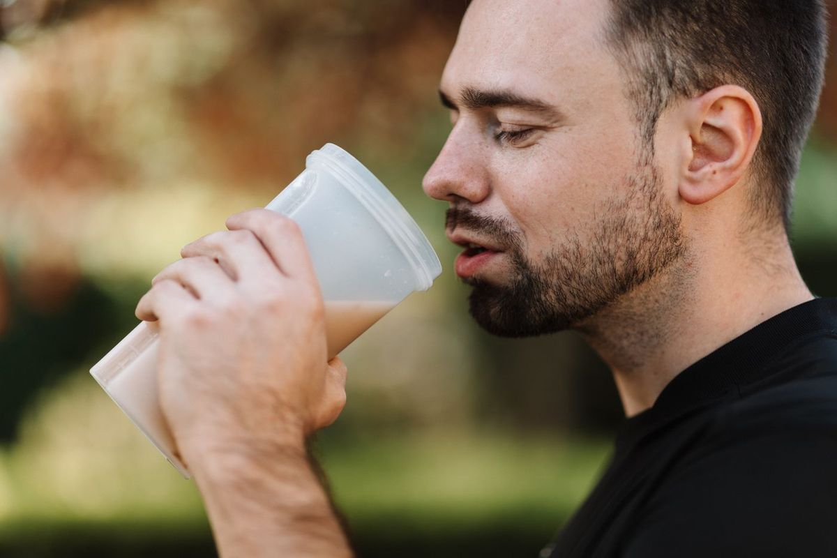 Uomo con la barba che beve un frullato da un bicchiere all'aperto