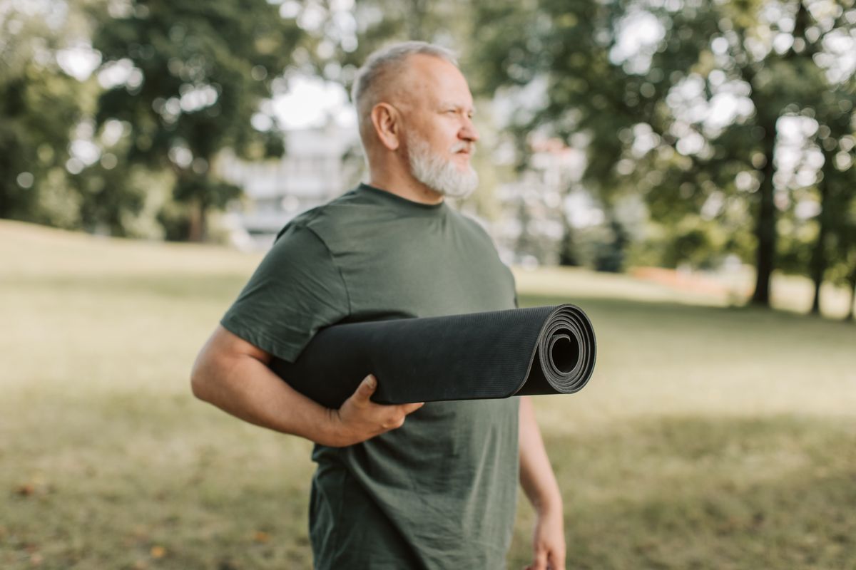 Uomo sulla cinquantina con un tappetino da yoga sotto il braccio in un parco